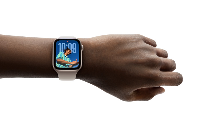 Närbild på Apple Watch i roséguld med armband i gummi på en persons handled för att visa upp den nya designen med Liquid Glass