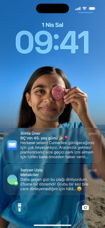 Hafifçe birbirinin üstüne binen beş iPhone modeli; en soldaki ekran, arka planı kişiselleştirilmiş bir Mesajlar sohbetini gösteriyor; soldan ikinci modelin ekranında renkli uygulama simgelerinin bulunduğu Ana Ekran görünüyor; ortadaki modelde, fotoğraflı Kilit Ekranı ve Liquid Glass efektiyle saat rakamları görünüyor, ekranın altında iki bildirim yer alıyor; sağdan ikinci modelde Liquid Glass efektli şeffaf uygulama simgeleri görünüyor; en sağdaki modelde ise Liquid Glass tasarımında bir müzik çalar yer alıyor