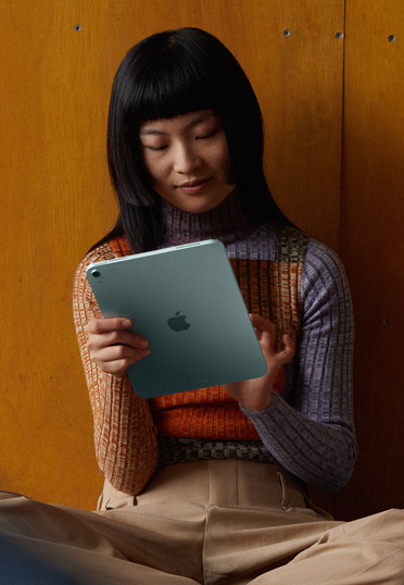 壁にもたれて床に座っている学生。手にiPadを持っている