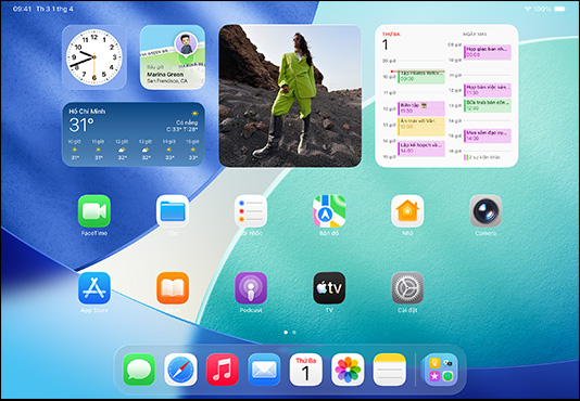 iPad, ba phiên bản, nằm ngang, với phiên bản ở giữa đặt trước hai phiên bản khác, Apple Pencil được gắn kết bằng nam châm vào phía trên của phiên bản ở giữa, màn hình ở giữa hiển thị Màn Hình Chính có các biểu tượng ứng dụng đầy màu sắc với hiệu ứng Liquid Glass, màn hình bên trái hiển thị ứng dụng Xem Trước, màn hình bên phải hiển thị Màn Hình Chính với các tệp xòe ra theo hình quạt từ dock